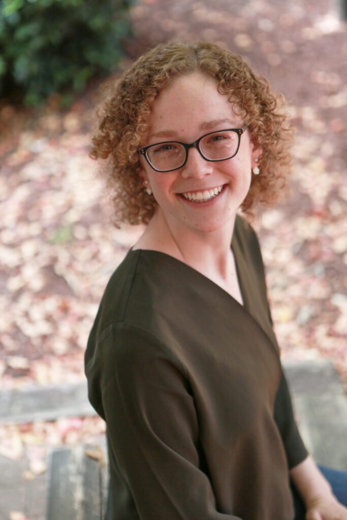 woman in green blouse with curly hair and glasses